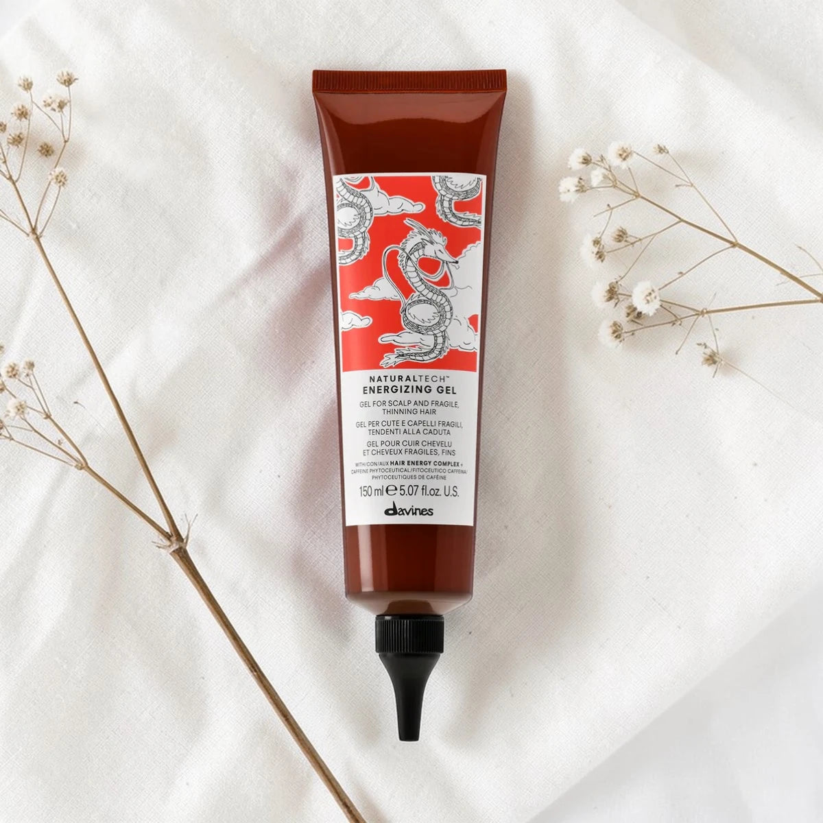 Tube de 150 ml du Naturaltech Energizing Gel de Davines, gel anti-chute pour cuir chevelu et cheveux fragiles au Hair Energy Complex et aux phytoceutiques de caféine, posé à plat sur un tissu blanc entouré de fleurs séchées.