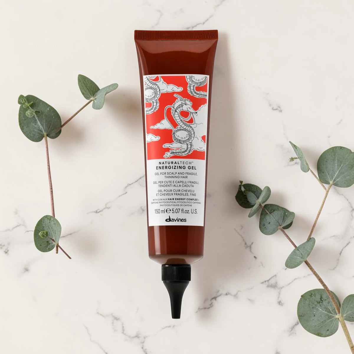Tube de 150 ml du Naturaltech Energizing Gel de Davines, gel anti-chute pour cuir chevelu et cheveux fragiles au Hair Energy Complex et aux phytoceutiques de caféine, posé à plat sur un plan en marbre entouré de feuilles d'eucalyptus.