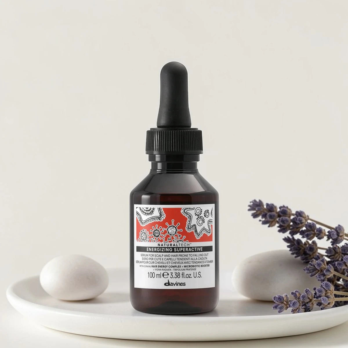 Flacon compte-gouttes de 100 ml du Naturaltech Energizing Superactive de Davines, sérum anti-chute pour cuir chevelu et cheveux fragiles au Hair Energy Complex et Microbiotic Booster, présenté sur une coupelle blanche avec des galets et des brins de lavande.