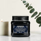 Pot noir de 250 ml du Heart of Glass Rich Conditioner de Davines, après-shampooing fortifiant et sublimateur pour cheveux blonds au Biacidic Bond Complex et à l'extrait de Jagua bleu, posé sur un plan en marbre aux côtés d'une bougie blanche et de feuilles d'eucalyptus.