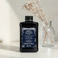 Flacon noir de 250 ml du Heart of Glass Silkening Chelating Shampoo de Davines, shampooing sublimateur pour cheveux blonds à l'extrait de Jagua bleu, posé sur une surface blanche aux côtés d'un vase en verre contenant des fleurs séchées.