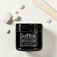 Pot noir de 250 ml du OI Hair Butter de Davines, baume de beauté absolue pour tous types de cheveux à l'huile de Roucou, posé sur une surface claire aux côtés de galets blancs et d'une spatule en bois.