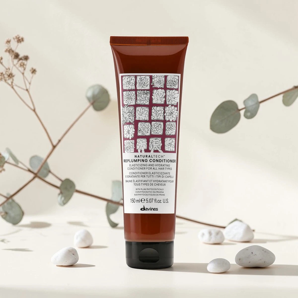 Tube de 150 ml du Naturaltech Replumping Conditioner de Davines, après-shampooing élastifiant et hydratant pour tous types de cheveux, aux phytoceutiques de prune, entouré de feuilles d'eucalyptus et de galets blancs.