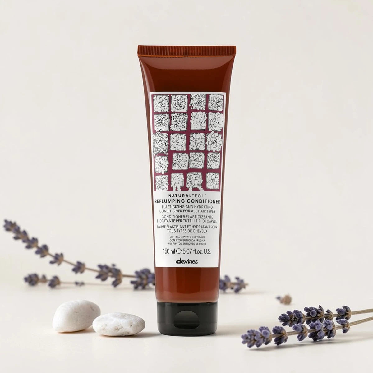 Tube de 150 ml du Naturaltech Replumping Conditioner de Davines, après-shampooing élastifiant et hydratant pour tous types de cheveux, aux phytoceutiques de prune, entouré de brins de lavande et de galets blancs.