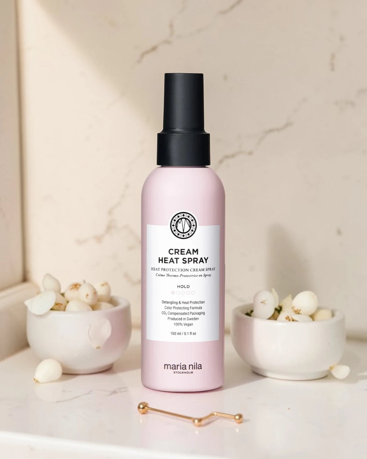 Bouteille de spray thermique crème Maria Nila sur une surface en marbre avec des éléments décoratifs
