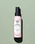 Flacon de spray chauffant crème avec étiquette rose sur fond vert clair