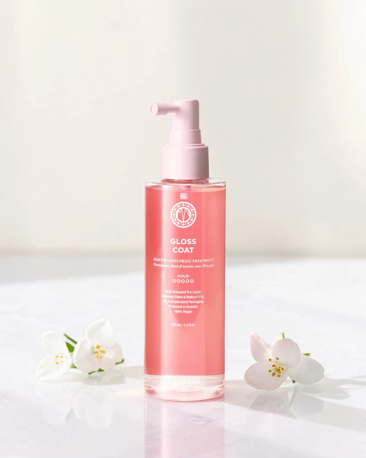 Bouteille rose étiquetée "Gloss Coat" avec des fleurs blanches sur un fond clair