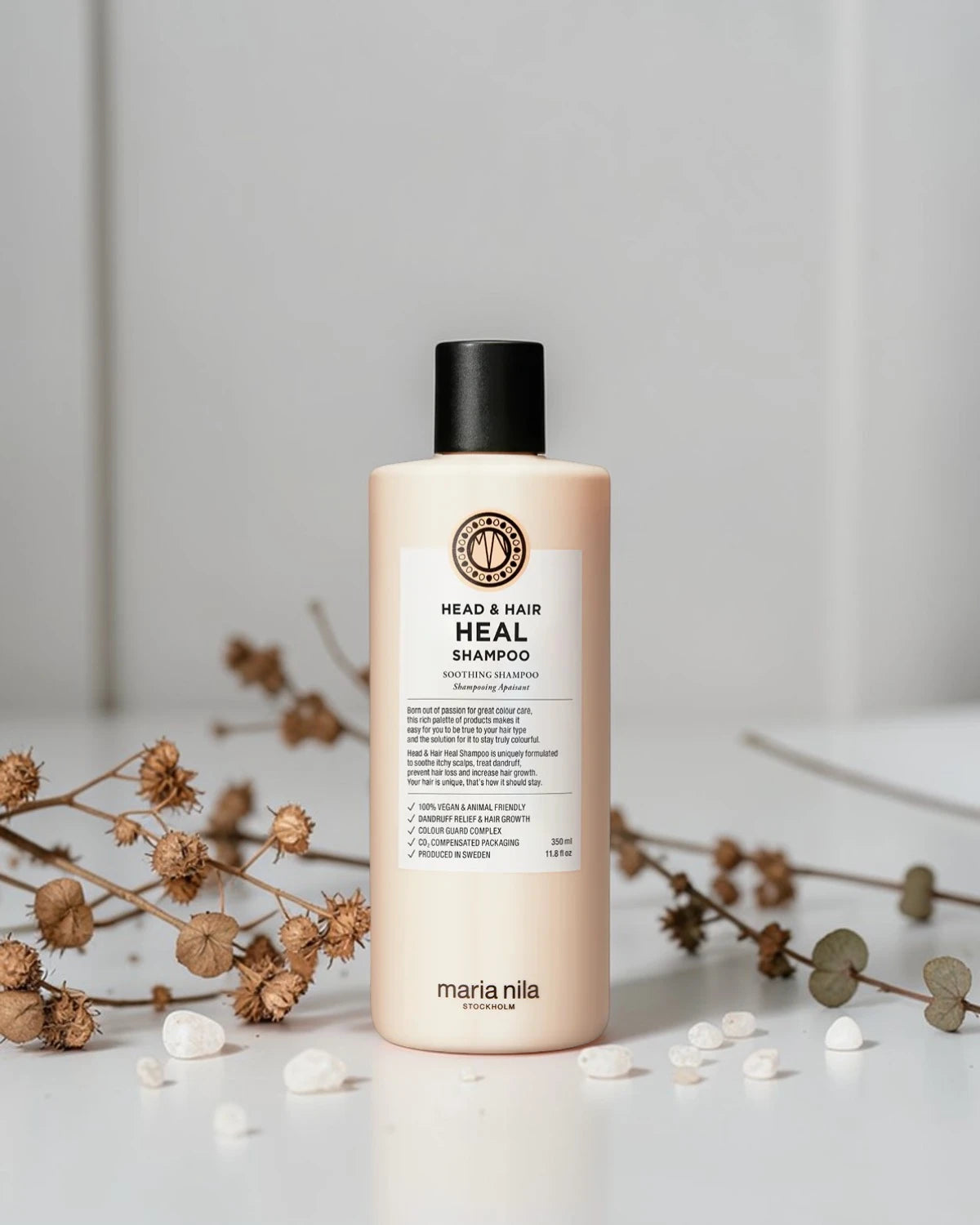 Shampoing Maria Nila Head & Hair Heal sur fond gris clair avec fleurs séchées et galets blancs, Victor Bazin Paris