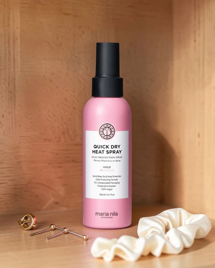 Flacon spray rose étiqueté 'Quick Dry Heat Spray' sur une surface en bois avec accessoires pour cheveux