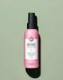 Flacon spray rose étiqueté "Quick Dry Heat Spray" par Maria Nila sur un fond vert clair