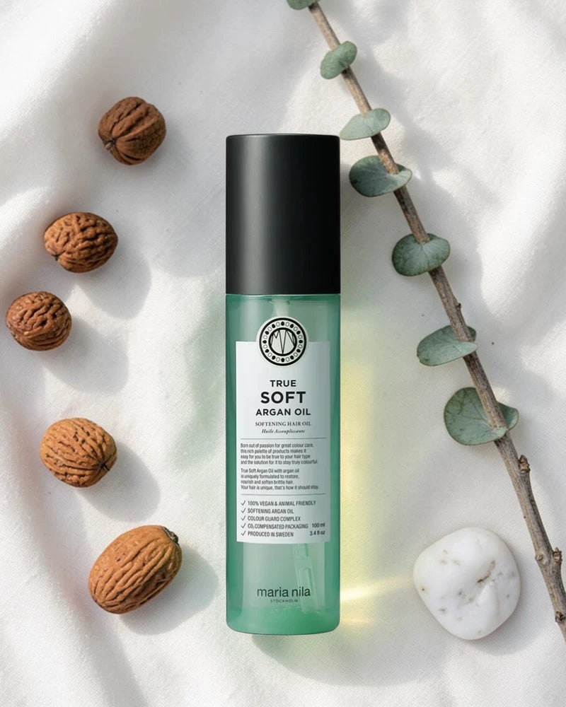 Bouteille verte étiquetée 'True Soft Argan Oil' avec des noix et une branche sur un fond clair