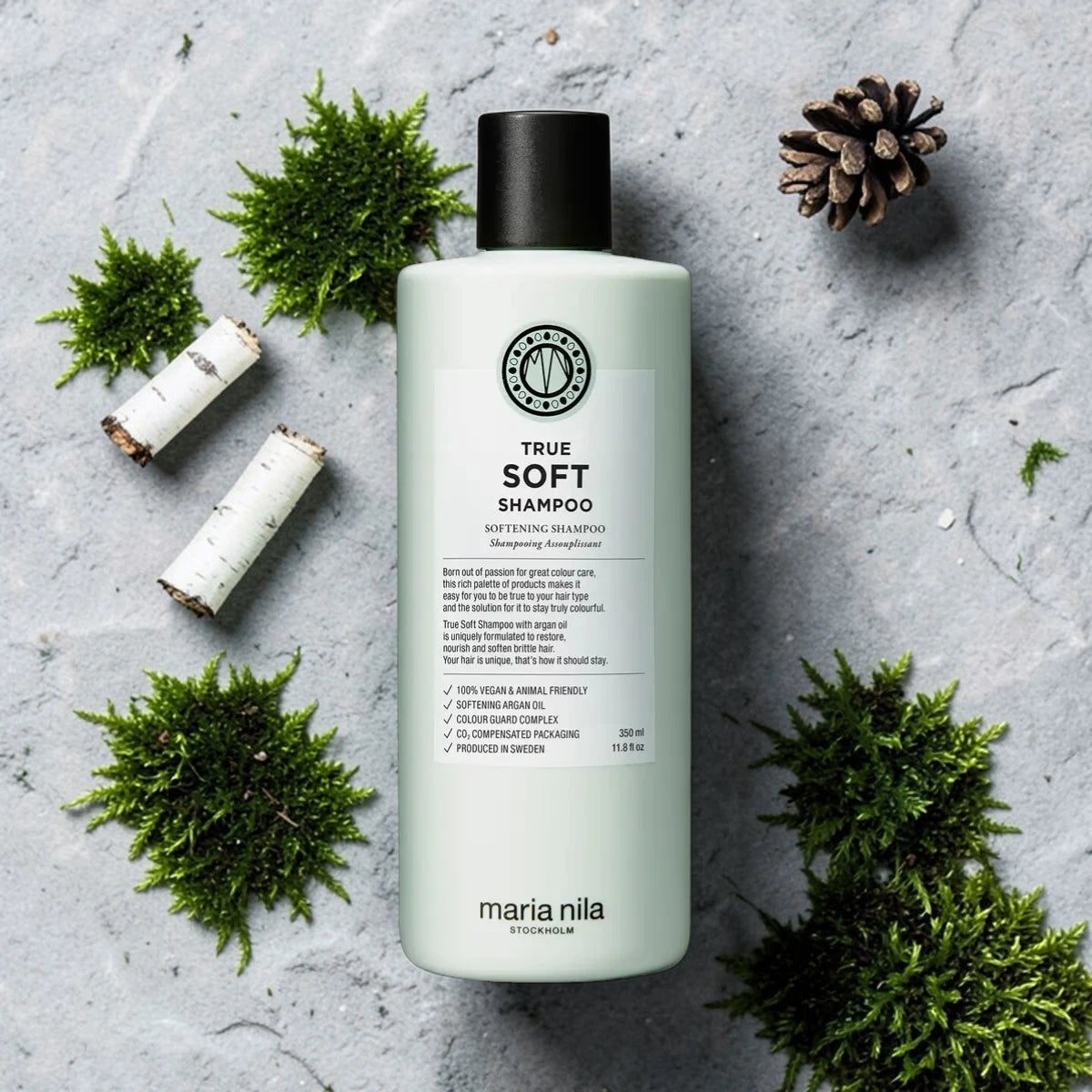 Bouteille de shampooing étiquetée 'True Soft Shampoo' par maria nila sur une surface texturée avec de la verdure