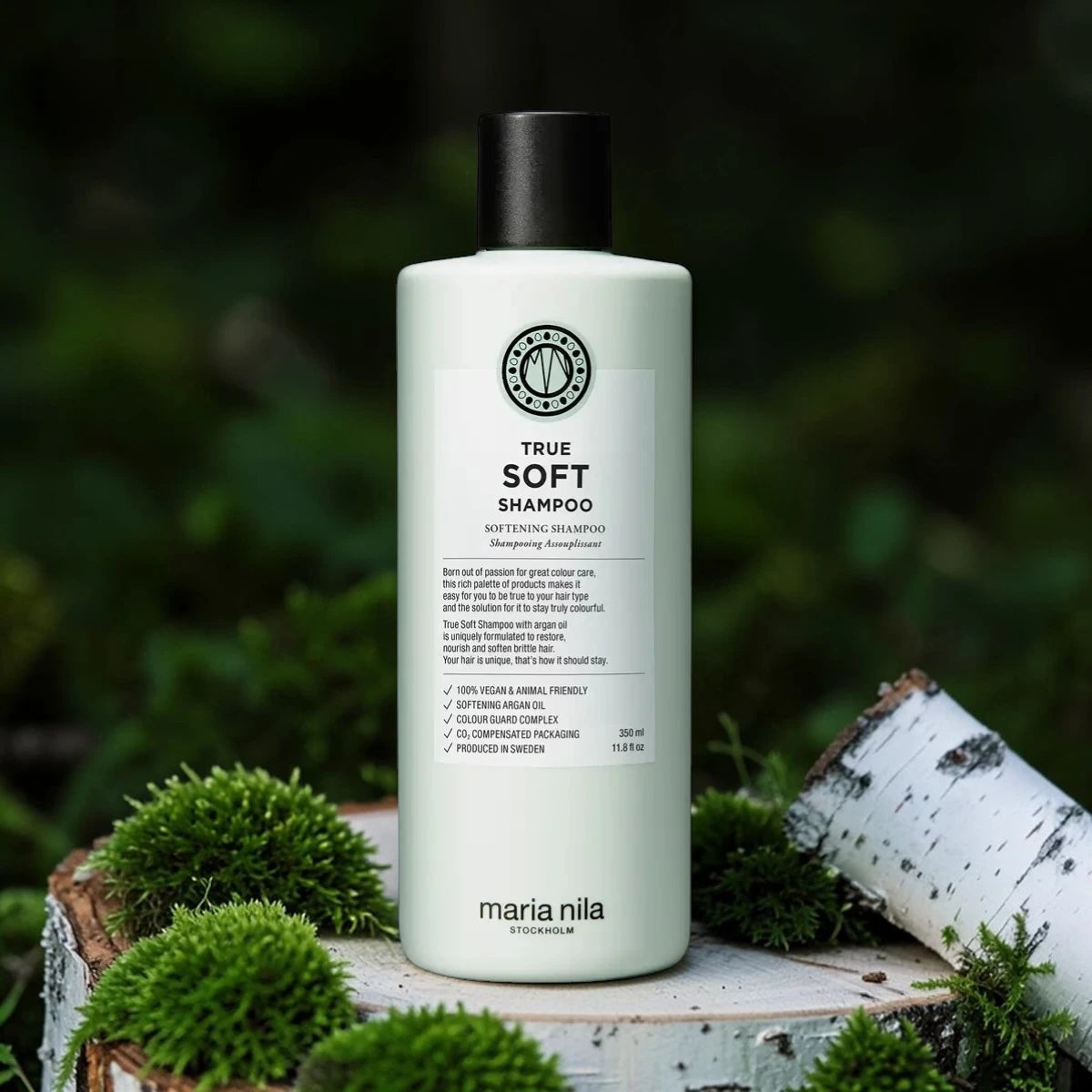 Bouteille de shampooing étiquetée 'True Soft Shampoo' par maria nila sur une surface en bois avec de la verdure en arrière-plan