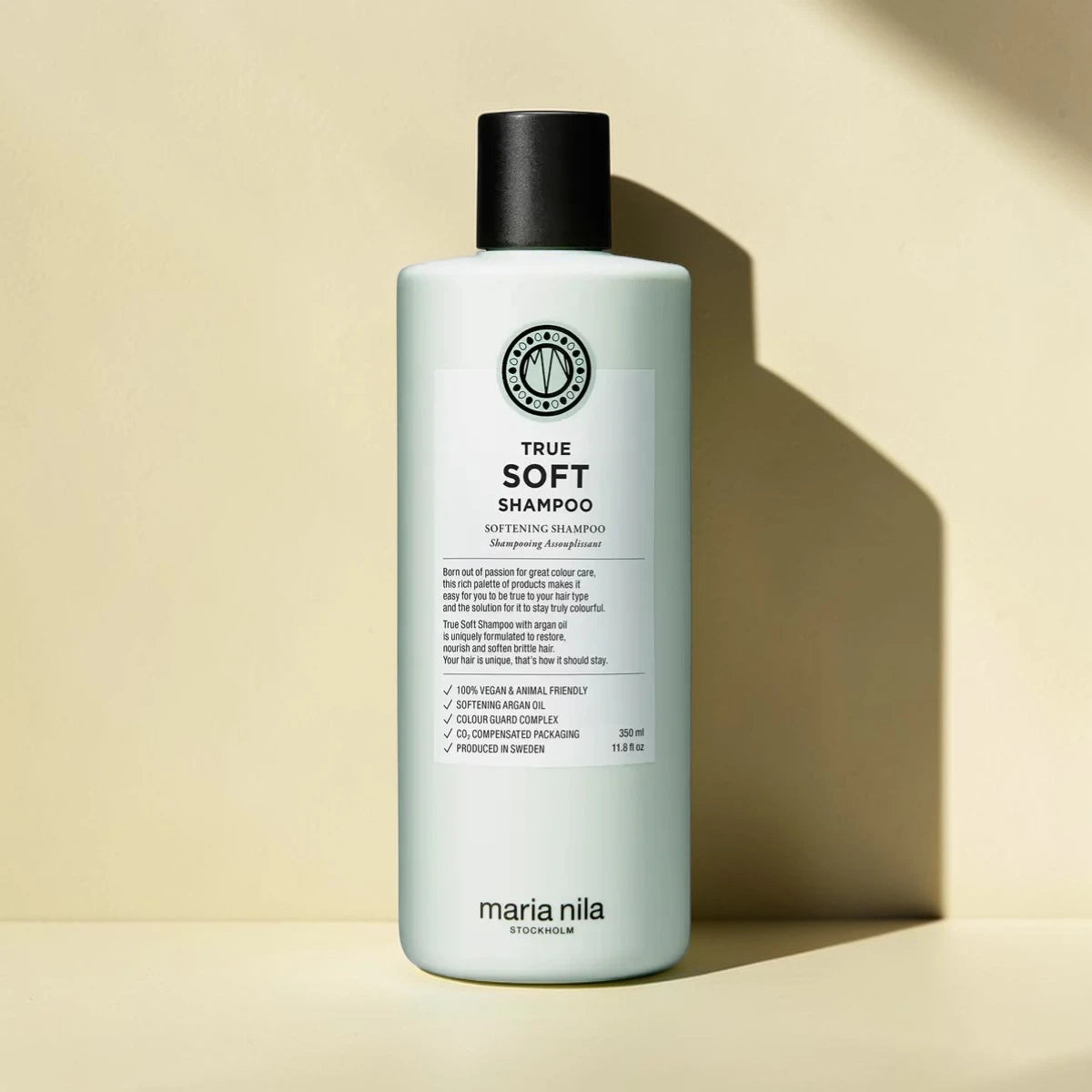 Bouteille de shampooing étiquetée "True Soft Shampoo" par Maria Nila sur un fond beige