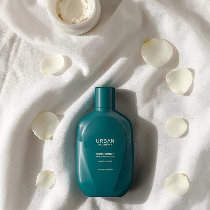 Flacon d’après-shampoing bleu étiqueté "Urban" sur un fond de tissu blanc avec des pétales éparpillés