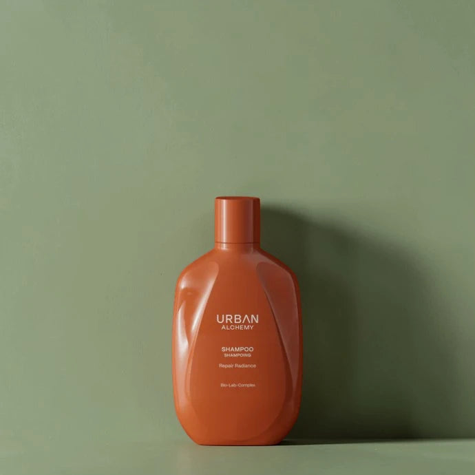 Bouteille de shampooing orange étiquetée 'Urban Alchemy' sur un fond vert