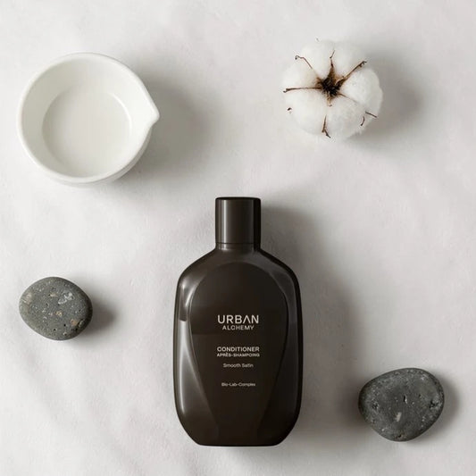 Flacon d’après-shampoing marron foncé étiqueté "Urban" sur un fond gris clair avec des éléments décoratifs
