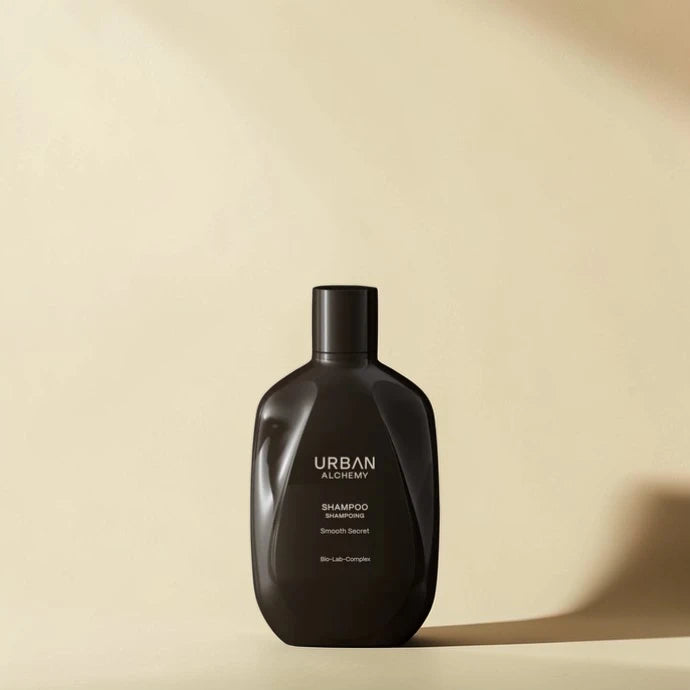 Bouteille de shampooing noir avec le logo 'Urban Alchemy' sur un fond beige