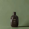 Flacon de shampoing marron foncé étiqueté "Urban Alchemy" sur fond vert