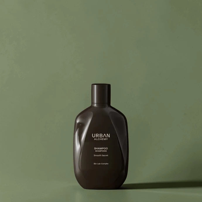 Flacon de shampoing marron foncé étiqueté "Urban Alchemy" sur fond vert