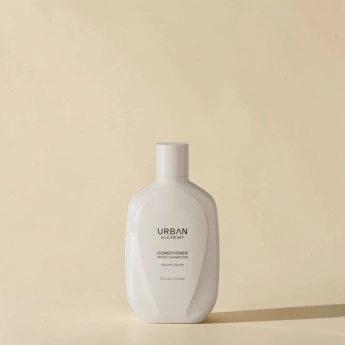 Flacon d’après-shampoing blanc étiqueté "Urban Alchemy" sur fond beige