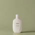 Bouteille blanche d’après-shampoing Urban Alchemy sur fond vert