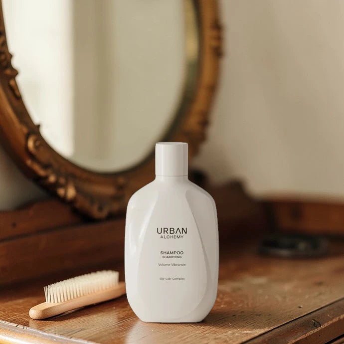 Bouteille de shampooing blanche étiquetée 'Urban Alchemy' sur une surface en bois avec un miroir en arrière-plan