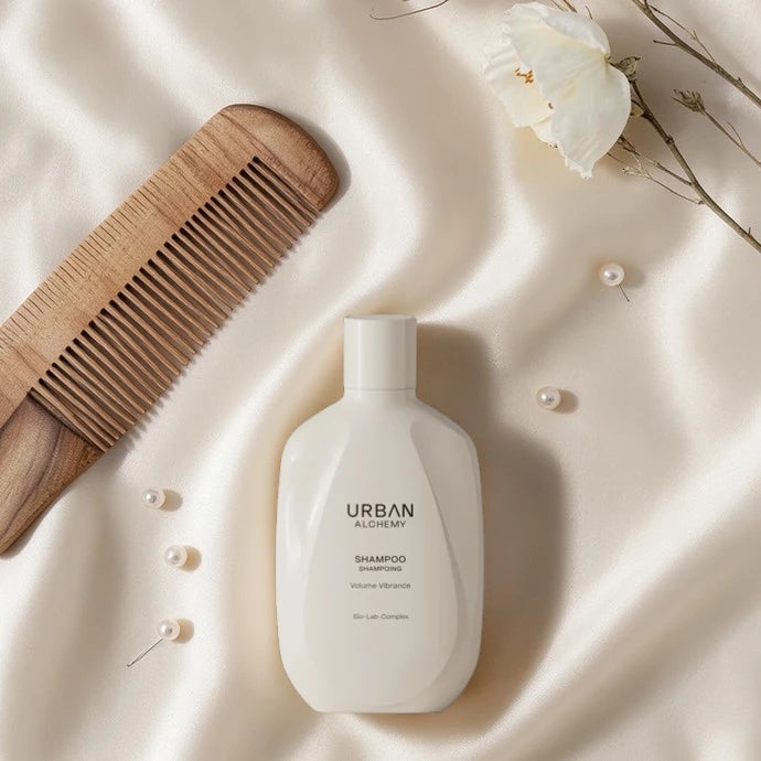 Bouteille de shampooing blanche étiquetée 'Urban Alchemy' avec un peigne en bois et des fleurs sur un fond clair