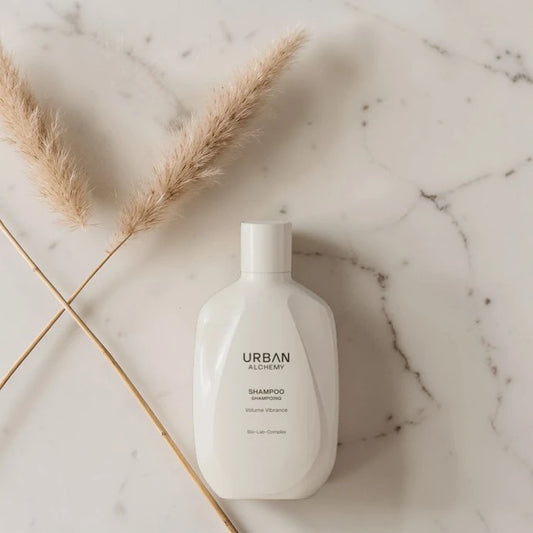 Bouteille de shampooing blanc étiquetée 'Urban Alchemy' sur une surface en marbre avec des herbes séchées