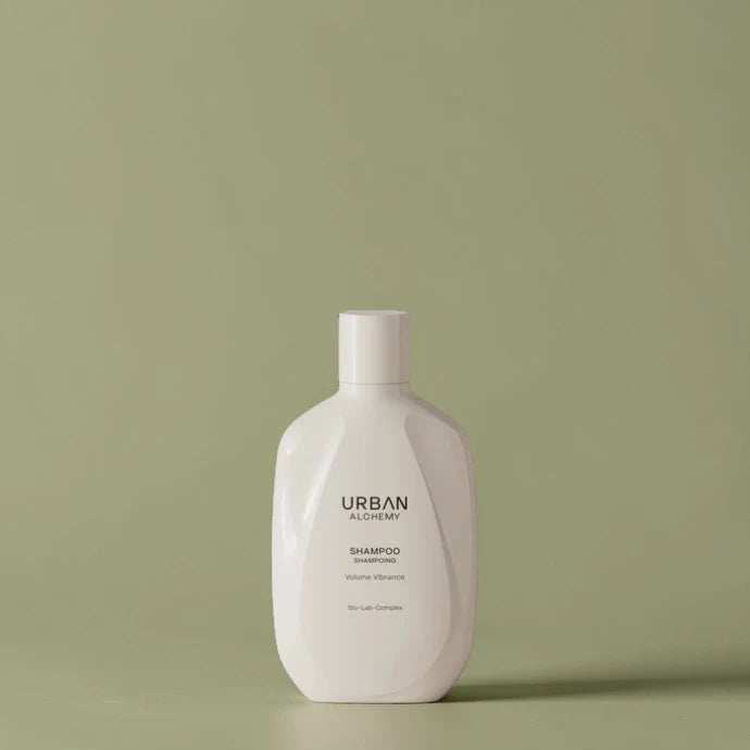 Flacon de shampooing blanc étiqueté "Urban Alchemy" sur fond vert clair